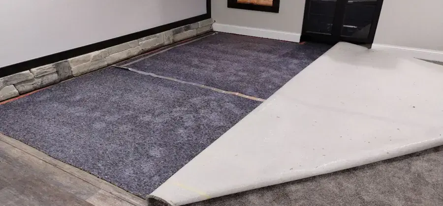 Wet carpet and pad peeled back from a finished basement floor
