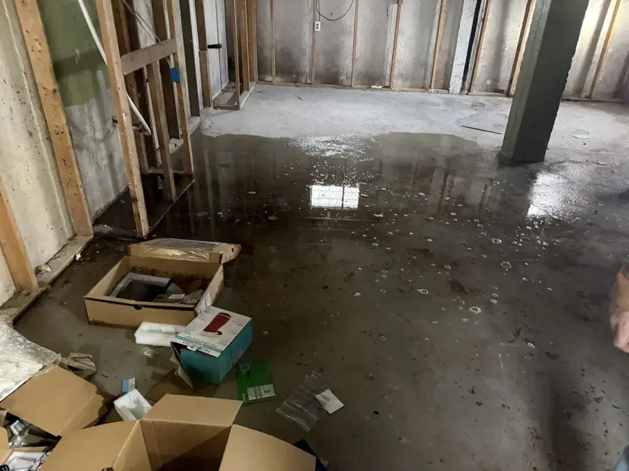 Standing water across an unfinished basement floor with framing and wet boxes