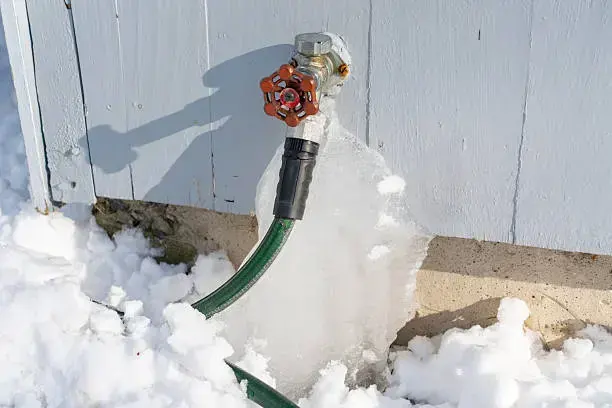 Frozen hose bib with a garden hose still attached and ice down the wall of a Riverton home