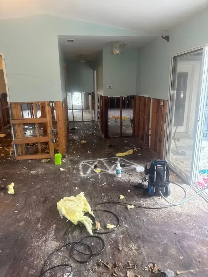 Sandy home hallway with lower drywall cut away, debris and drying gear on a bare floor