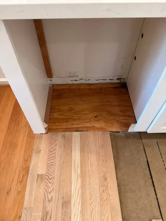 Dishwasher bay with a water-stained subfloor and damaged hardwood after an appliance leak in Riverton