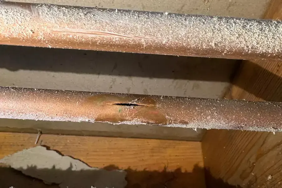 Frost-covered copper pipes in a joist bay, one split open by a hard Riverton freeze