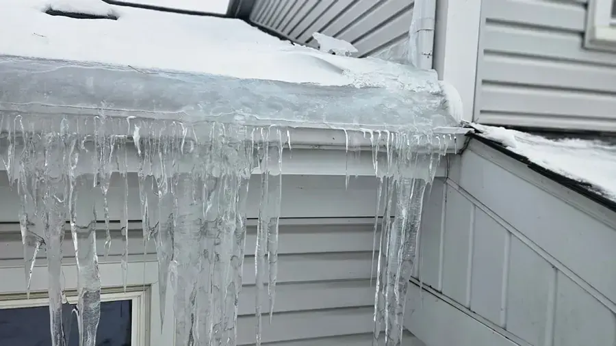 Ice dam and icicles along a snow-covered roof edge and gutter on a Riverton home